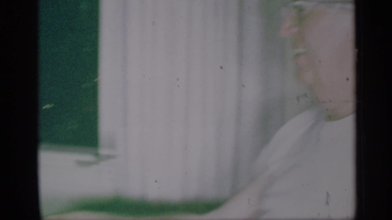 Soft, partially obscured view of an elderly man in glasses near curtains.