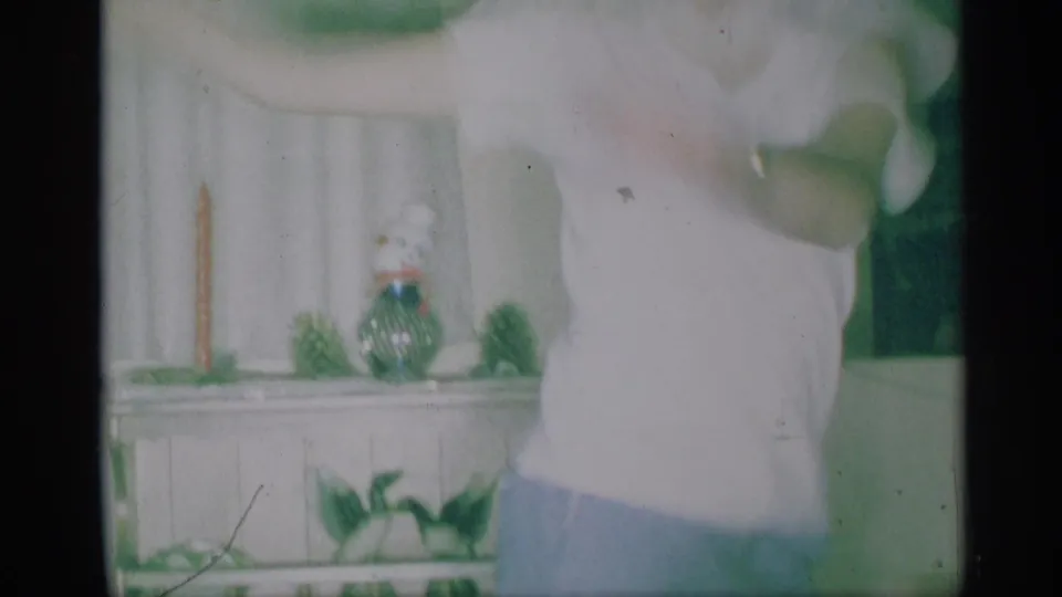 1959 New York home-movie frame with an older man partly framed beside a shelf holding small holiday decorations.