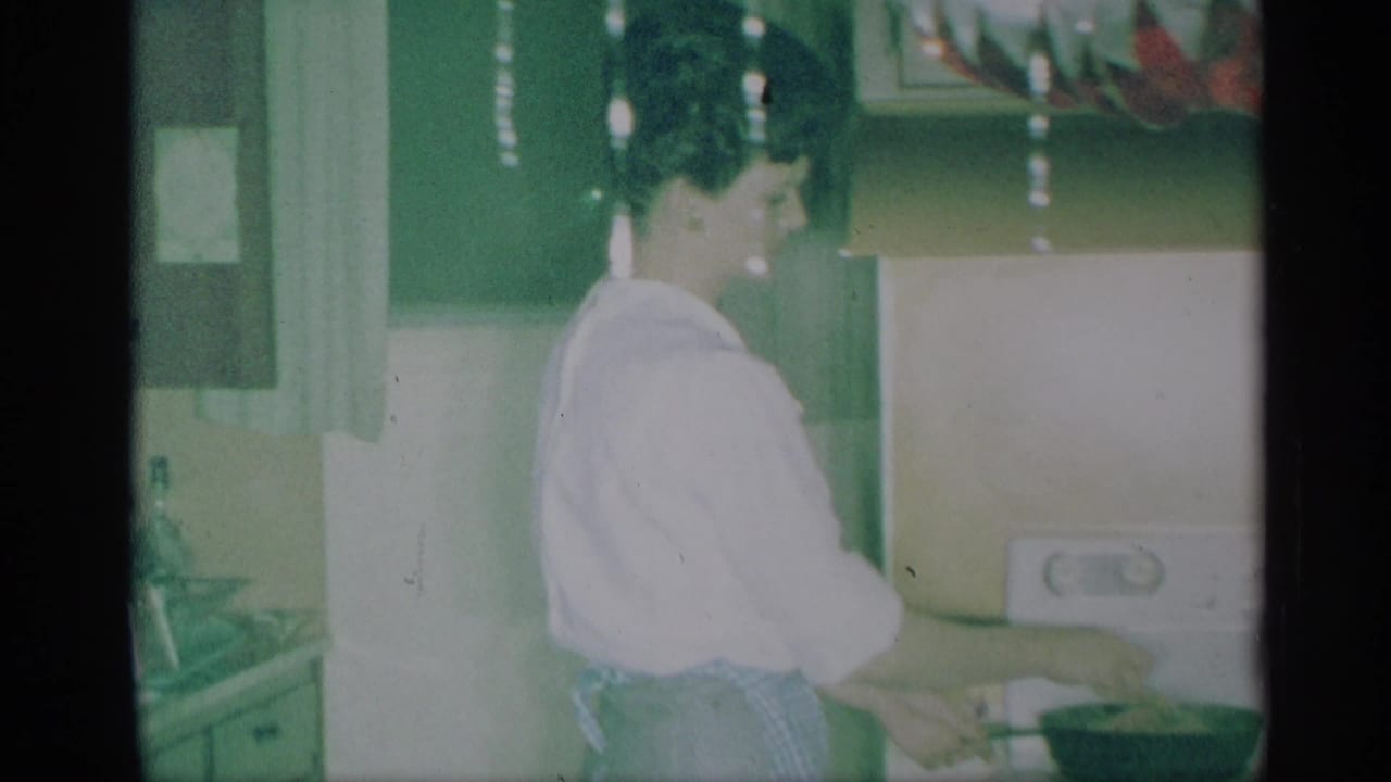 Woman in a light blouse stands at a kitchen counter near cabinets and holiday decor.