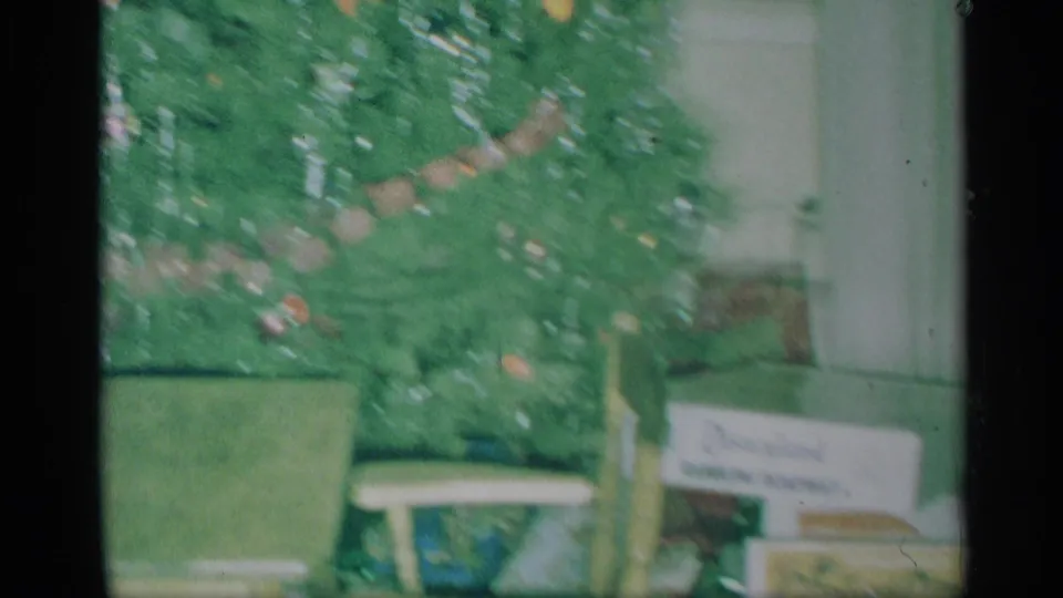 1959 New York home-movie frame showing a decorated Christmas tree, ornaments, and a visible Disneyland sign in a private room.