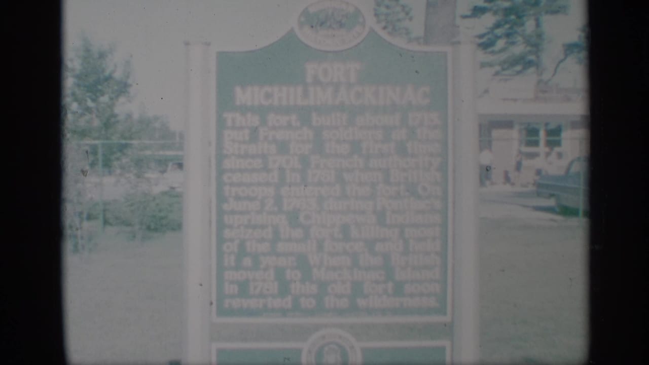 Green Fort Michilimackinac marker with outdoor grounds and a building behind it.