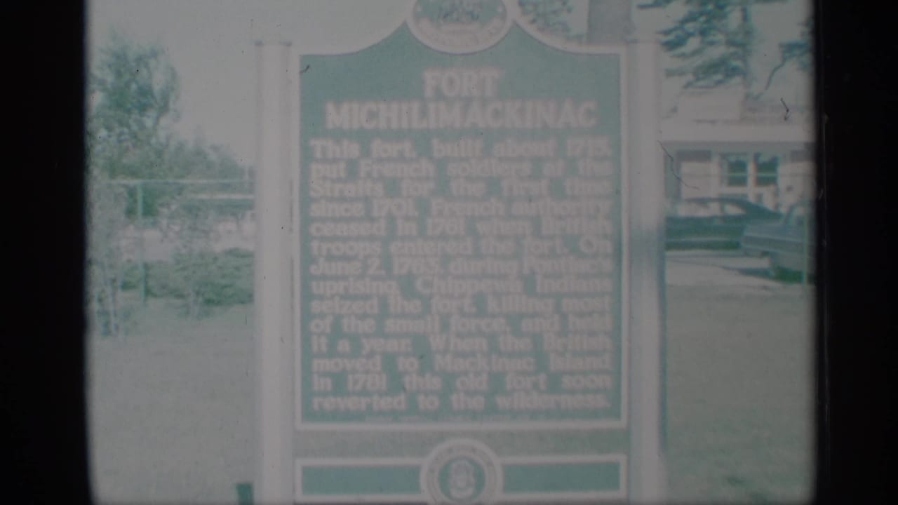 The final frame keeps the green Fort Michilimackinac marker in view, with lawn, trees, and a background building softened by faded 8mm color.