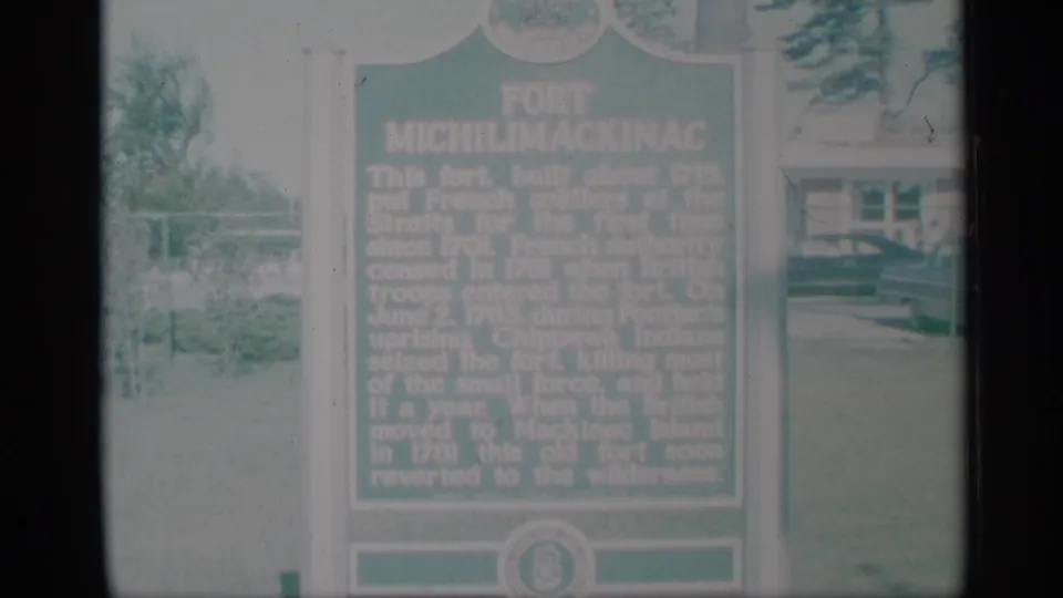 The final frame keeps the green Fort Michilimackinac marker in view, with lawn, trees, and a background building softened by faded 8mm color.