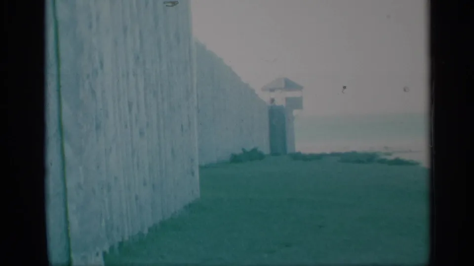 Visitor-shot 8mm view of a wooden palisade wall and distant guard tower at a preserved historic site in 1959.