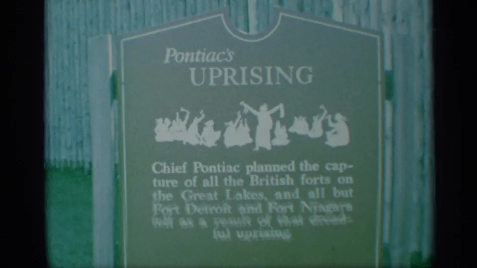 1959 New York 8mm footage shows a green Pontiac's Uprising historical marker with white lettering, partly blurred beside vertical wooden fencing.