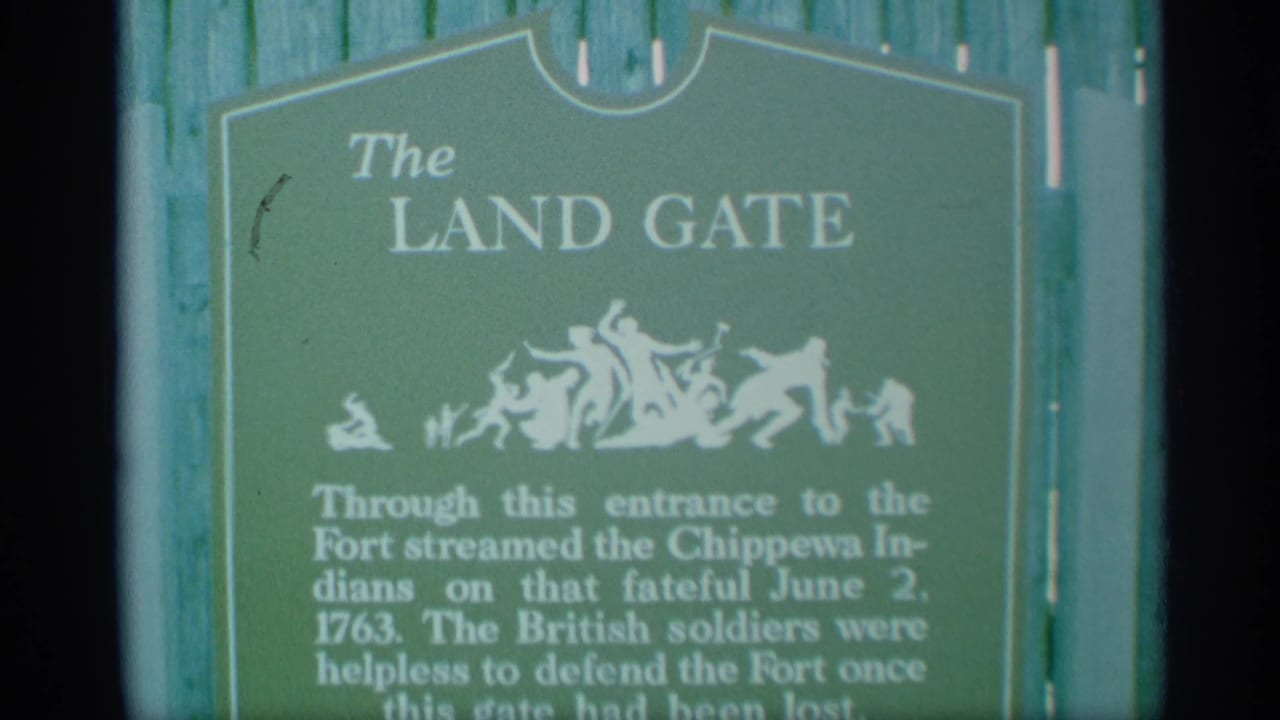 1959 New York home-movie frame shows The Land Gate marker at a fort, with white lettering, silhouette art, and text mentioning Chippewa Indians.