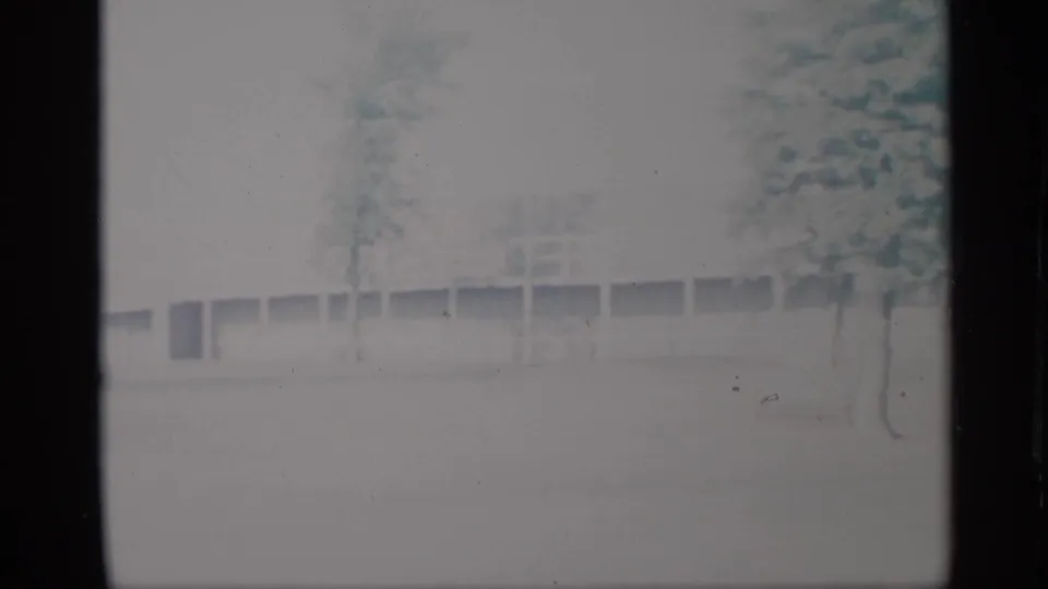 Soft 8mm frame from 1959 New York showing a pale building facade, trees, and indistinct open grounds.