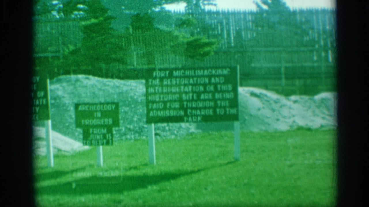 Green signs on grass in front of earth piles and a wooden fort fence.