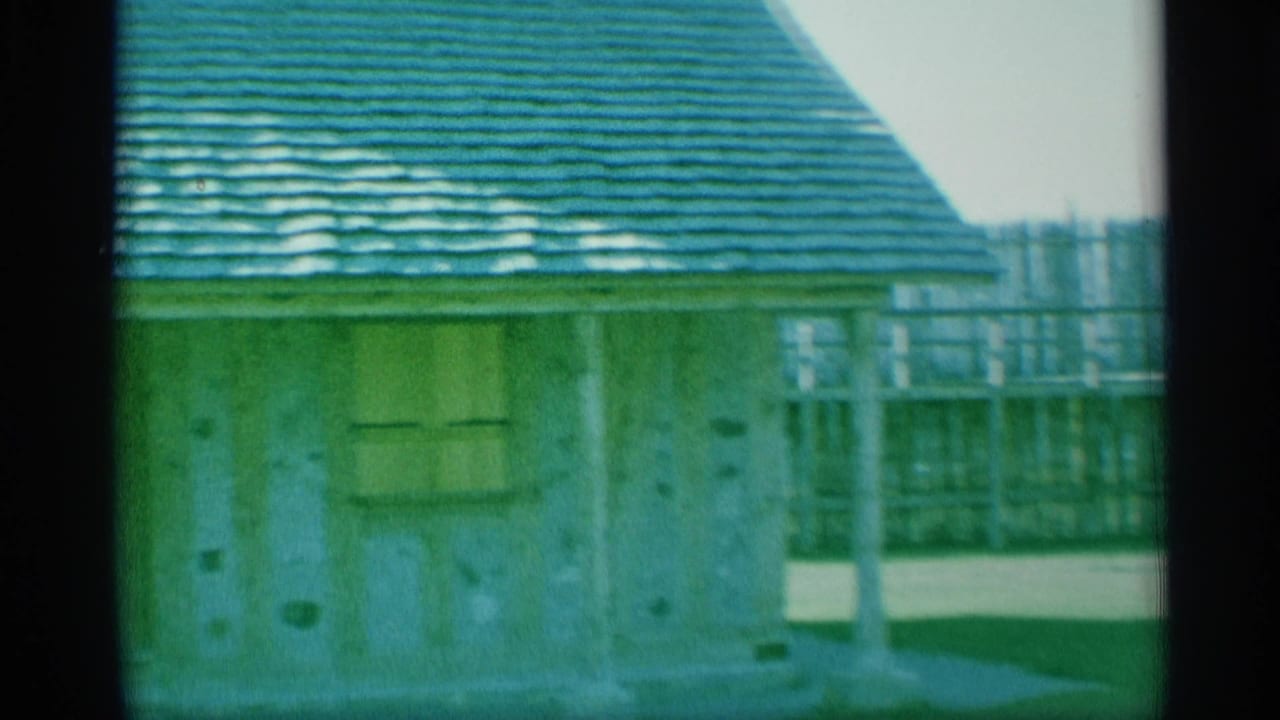 1959 New York 8mm frame showing a small weathered building with a green shingled roof near a sparse waterfront area.