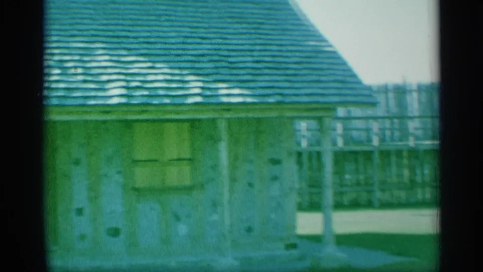 1959 New York 8mm frame showing a small weathered building with a green shingled roof near a sparse waterfront area.