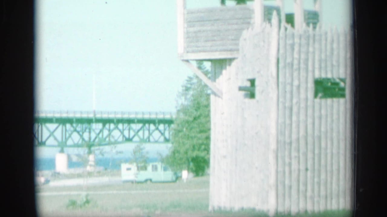 1959 New York waterfront view with a wooden lookout structure, long truss bridge, parked vehicle, and distant water.