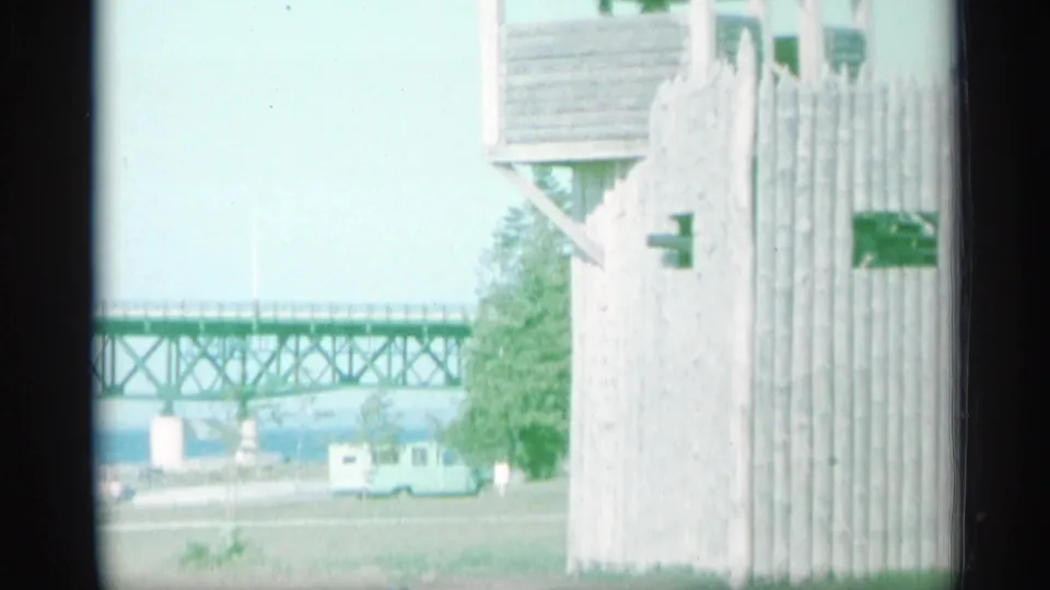 1959 New York waterfront view with a wooden lookout structure, long truss bridge, parked vehicle, and distant water.