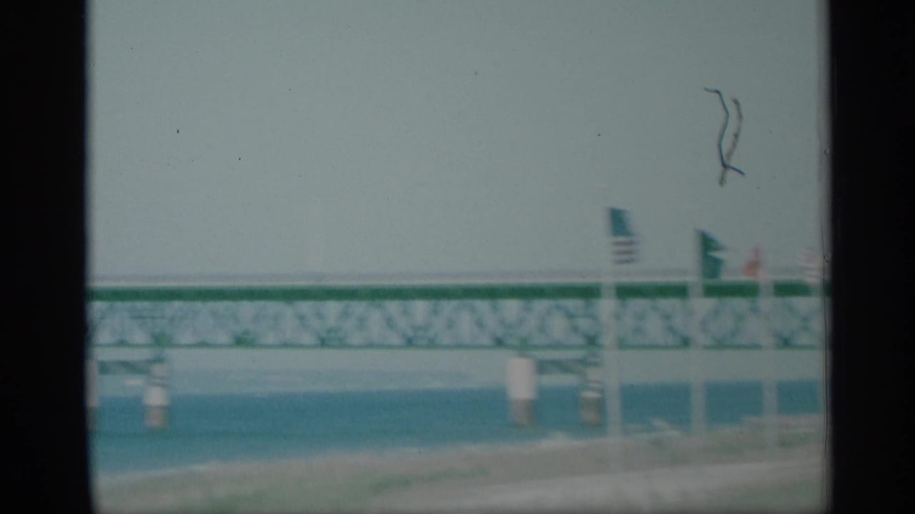 1959 New York waterfront frame showing a long truss bridge over water, flags, shoreline, and soft home-movie exposure.