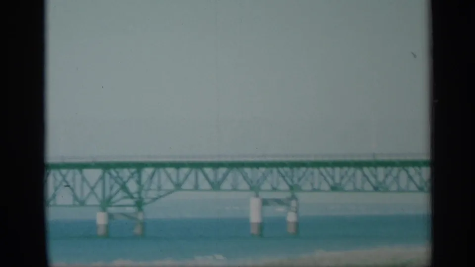 1959 New York 8mm frame showing a distant green truss bridge spanning blue water under a pale sky.