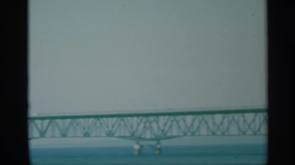 Distant 1959 New York bridge view with green truss spans, water below, and soft sky above.