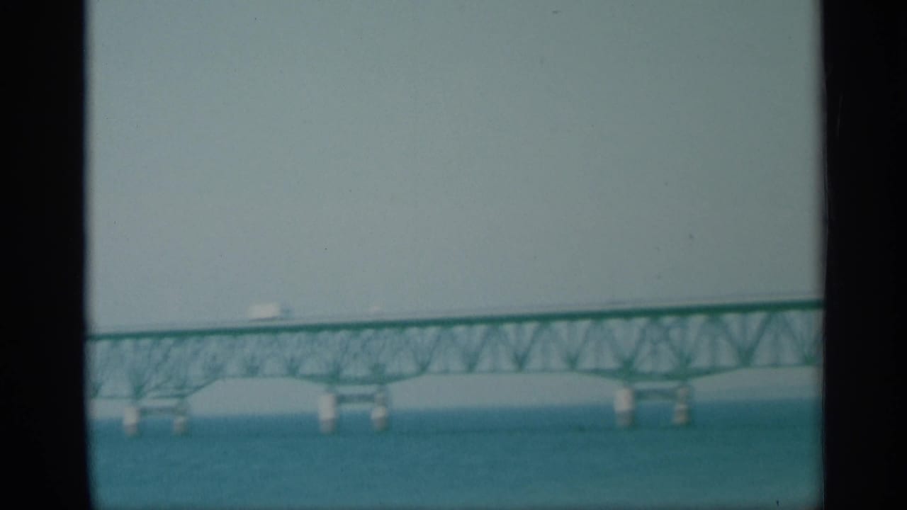 Soft 8mm frame from 1959 New York showing the lower bridge span, water, and a pale sandy foreground.