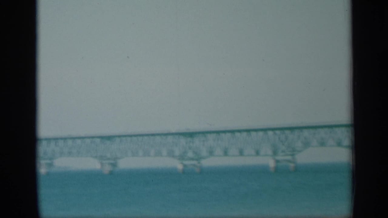 1959 New York 8mm view of a green truss bridge crossing blue water with supports visible below.