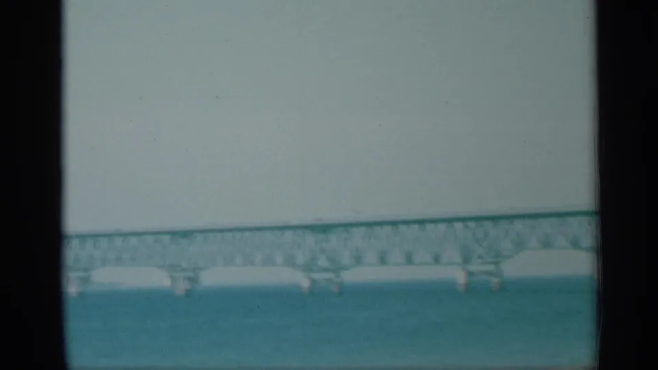 1959 New York 8mm view of a green truss bridge crossing blue water with supports visible below.