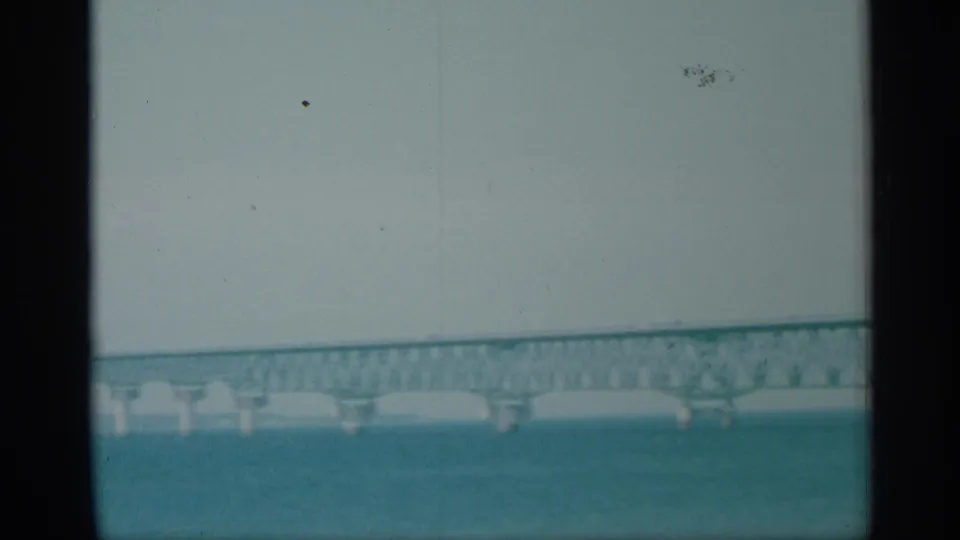1959 New York 8mm frame showing a distant bridge span over wide blue-green water with dark film borders.