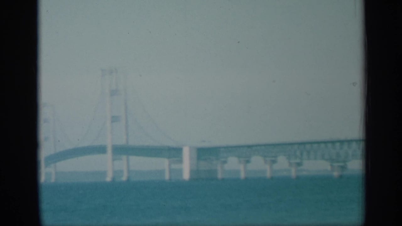 1959 New York 8mm frame with suspension bridge towers, cables, and roadway seen across a broad river.