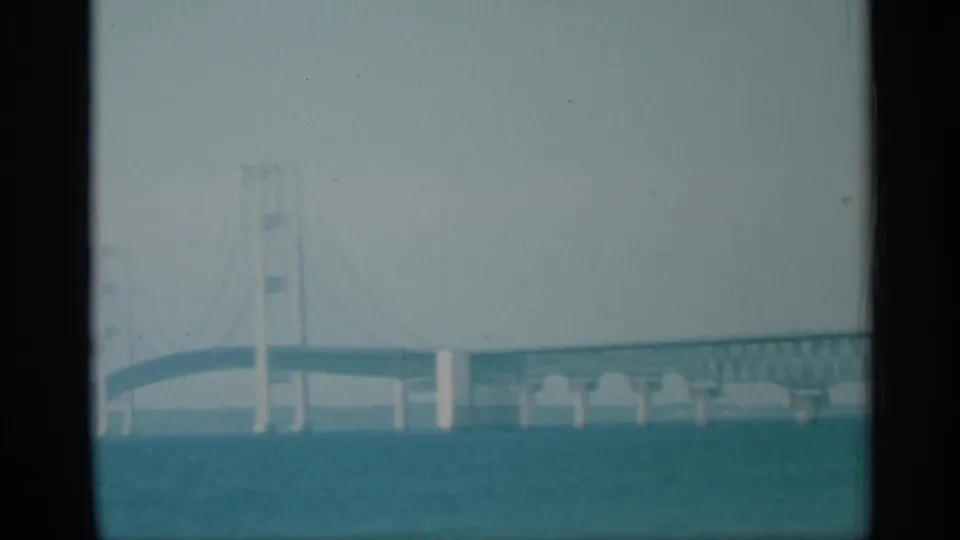 1959 New York 8mm frame with suspension bridge towers, cables, and roadway seen across a broad river.