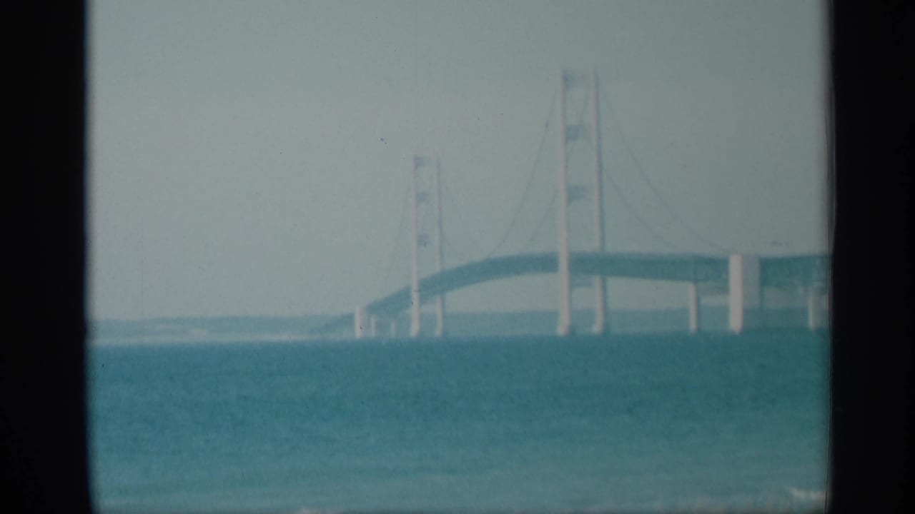 Distant suspension bridge over blue-green water seen through a film frame border.