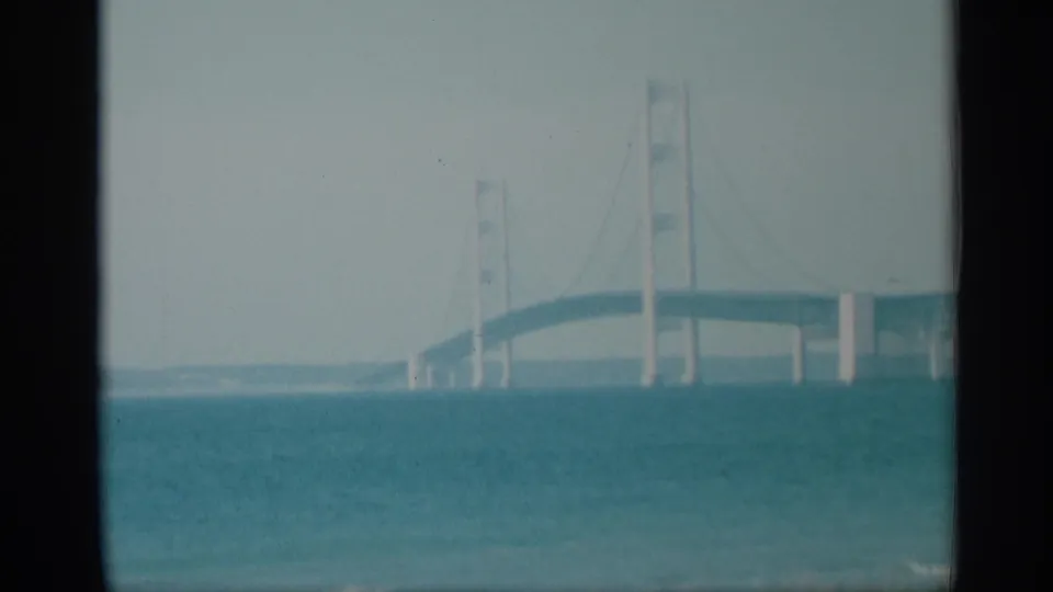 1959 8mm frame showing a distant suspension bridge across blue-green water, with soft exposure and dark film borders.