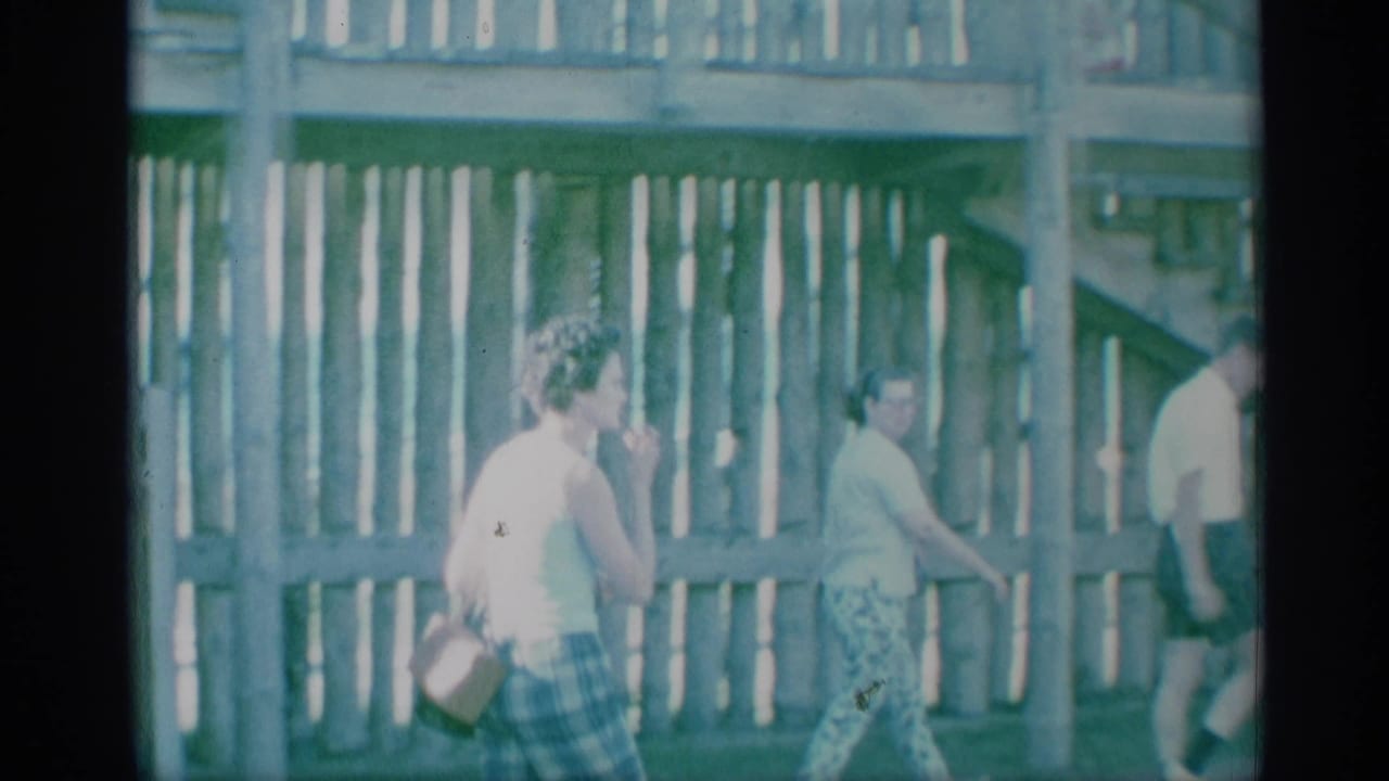 Adults walk beside a wooden stair structure in a faded 8mm frame.