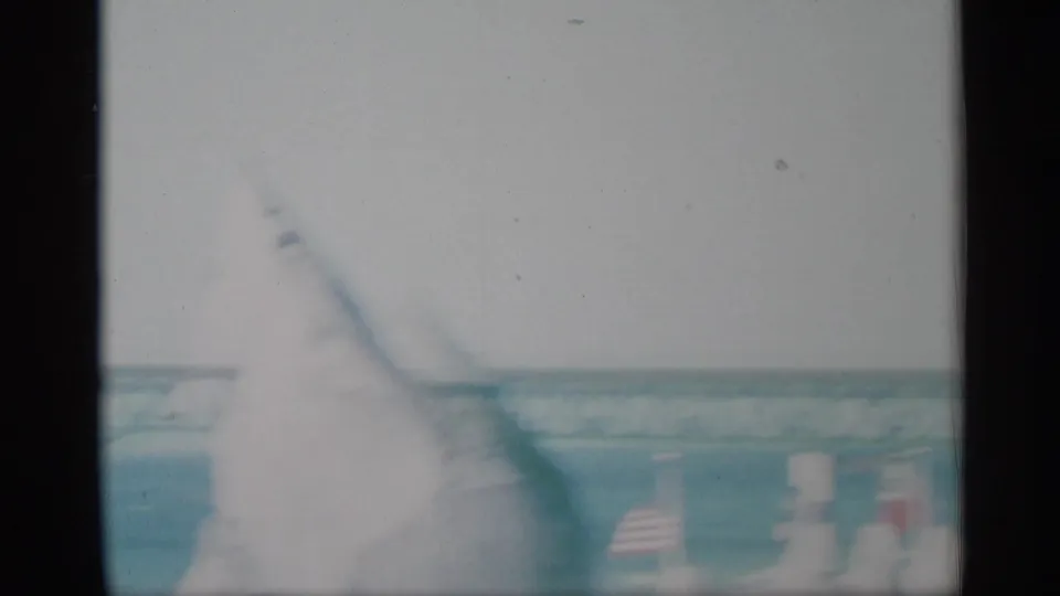 The camera shifts to a washed-out waterfront view with a distant bridge structure, water, and traffic cones in the foreground.