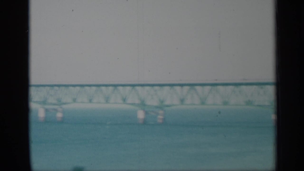 A faded 8mm view shows water in the foreground and a distant bridge crossing the New York waterfront.