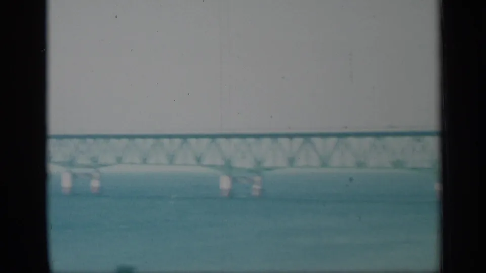 A faded 8mm view shows water in the foreground and a distant bridge crossing the New York waterfront.