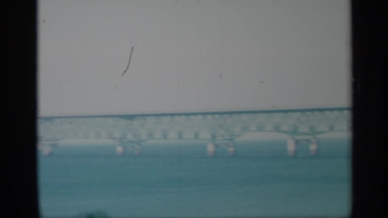 Long bridge crossing water behind dark vertical window divisions.