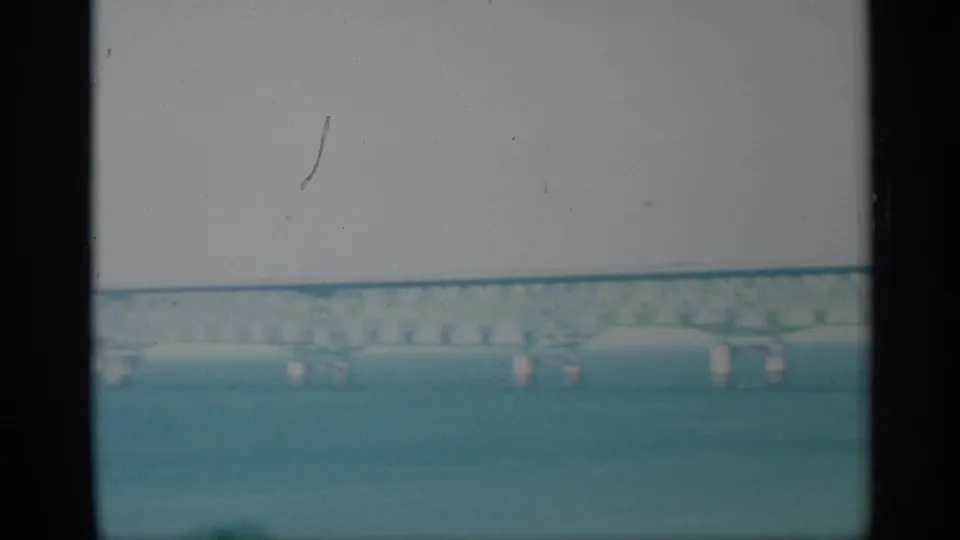 1959 New York 8mm frame showing a long bridge over water, seen through dark vertical divisions with hazy sky and faded color.