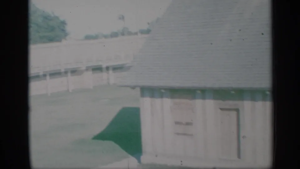 1959 New York home-movie view of the house corner, green-trimmed entry area, porch rail, lawn, and shingled roof.