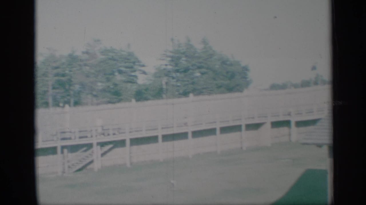 1959 New York frame showing a wooden fence, trees, lawn, and part of the shingled house roof in soft 8mm color.