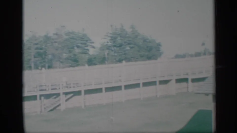 1959 New York frame showing a wooden fence, trees, lawn, and part of the shingled house roof in soft 8mm color.