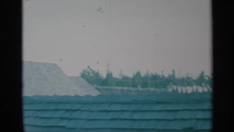 1959 New York 8mm frame with a broad shingled roof foreground, pale fort wall, distant trees, and a partial roof edge during the pan.