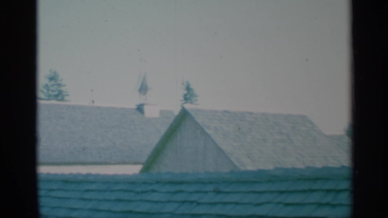 1959 New York 8mm frame showing steep fort rooftops and a small cupola-like feature above the roofline, with trees behind.