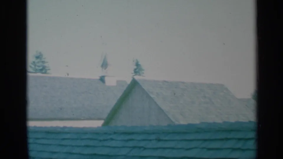 1959 New York 8mm frame showing steep fort rooftops and a small cupola-like feature above the roofline, with trees behind.