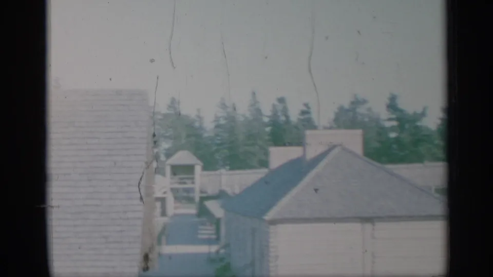 1959 New York 8mm frame showing a close wall, small roofed structure, house roof, evergreen trees, and faded film texture.