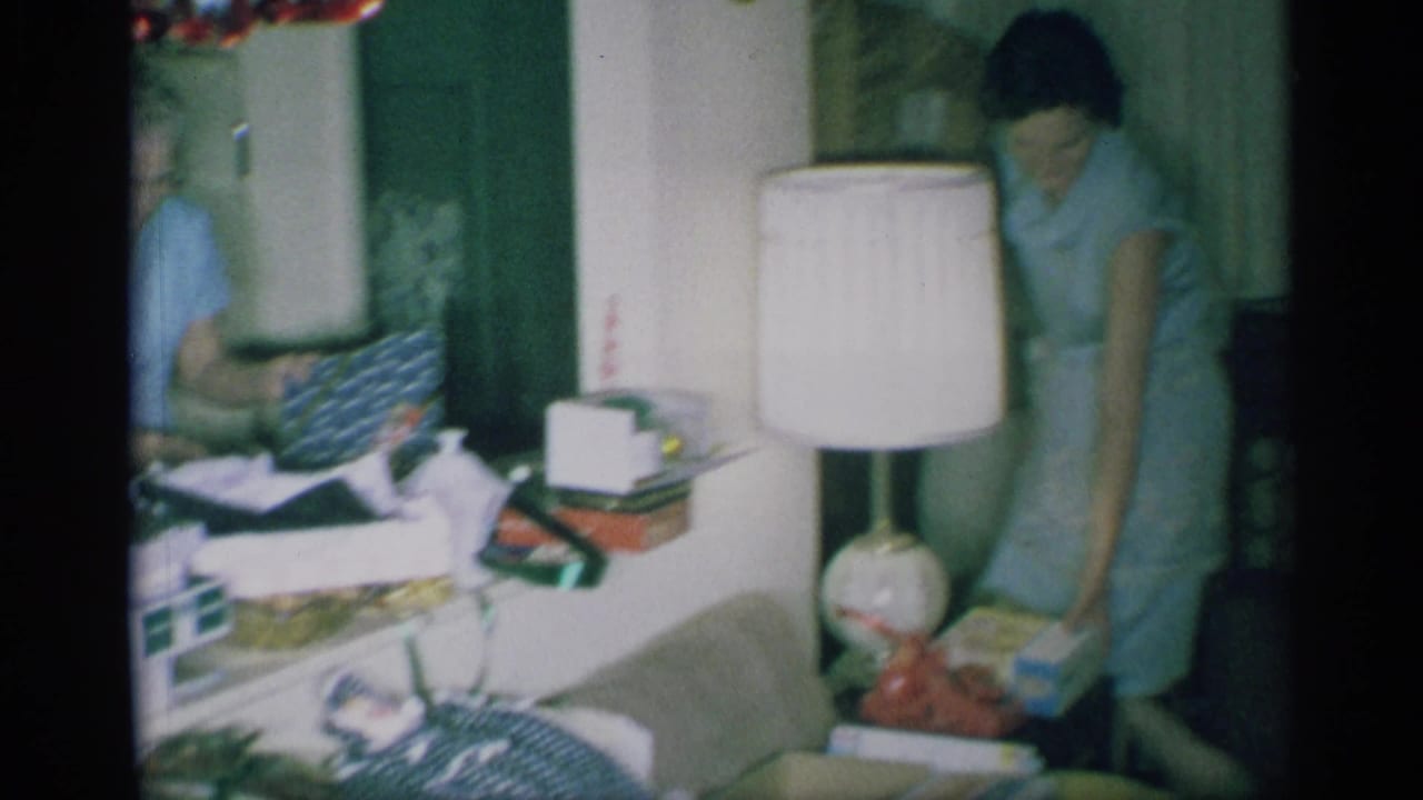 Woman in a light blue dress leans over gifts in a crowded living room.