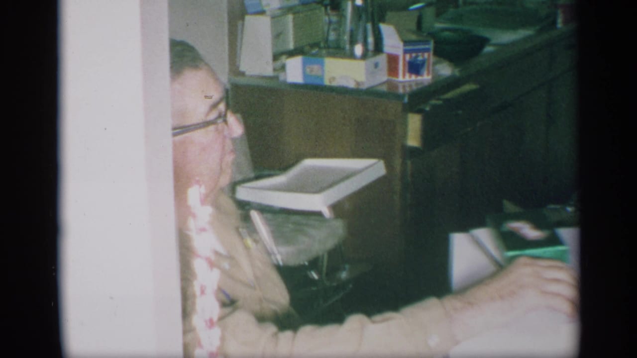 Man with glasses seated beside a kitchen counter, with a small tray chair in the background.