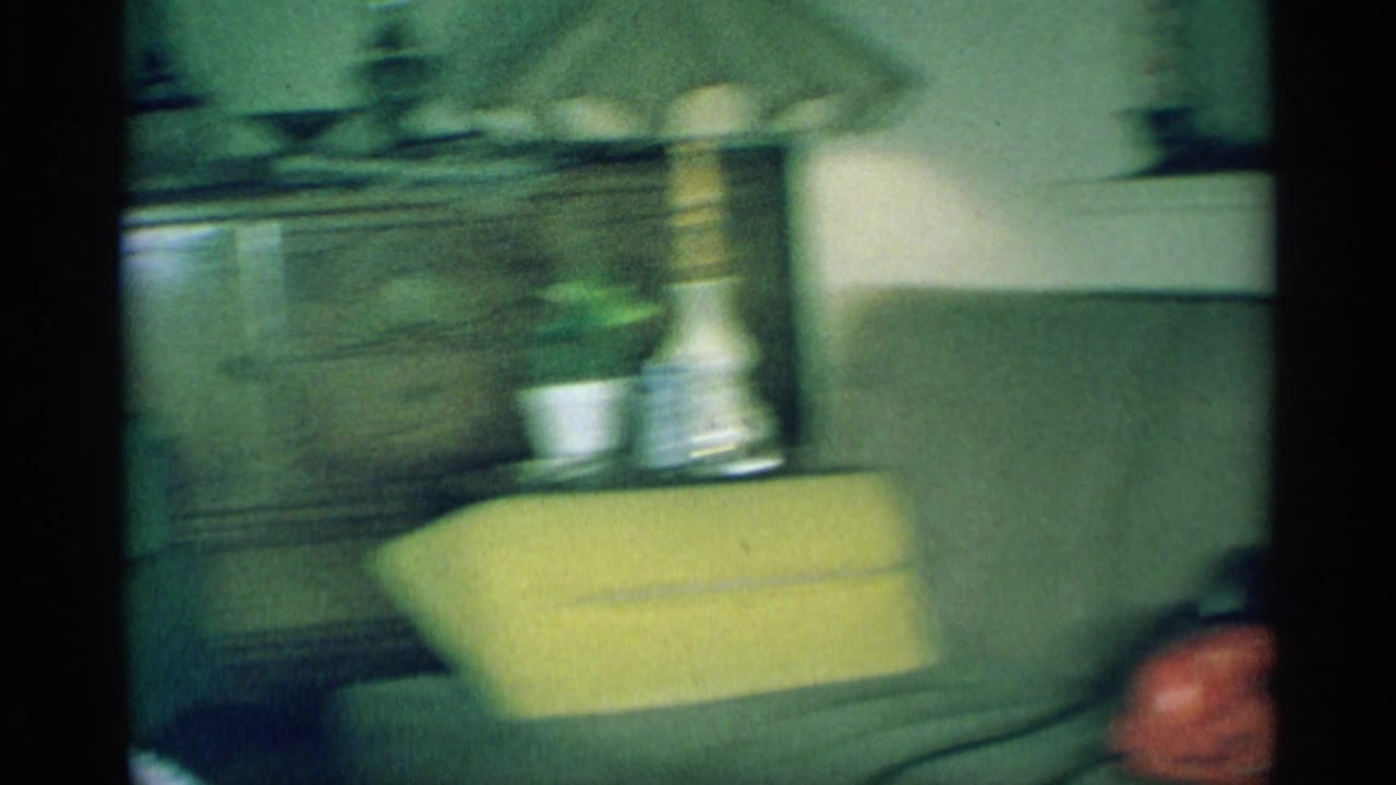 A blurred 1959 New York home interior frame shows a chair, lamp, cabinet, and furnishings during a quick handheld camera move.