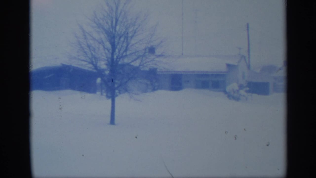 1959 New York home-movie frame showing a snowy residential exterior, bare tree, utility pole, and low roofline.