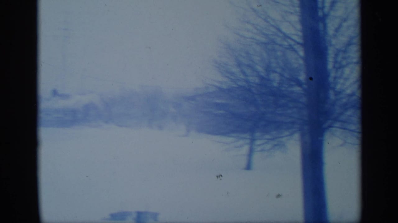 1959 New York winter landscape with snow, leafless trees, faint distant buildings, and heavy dark film or window edges.