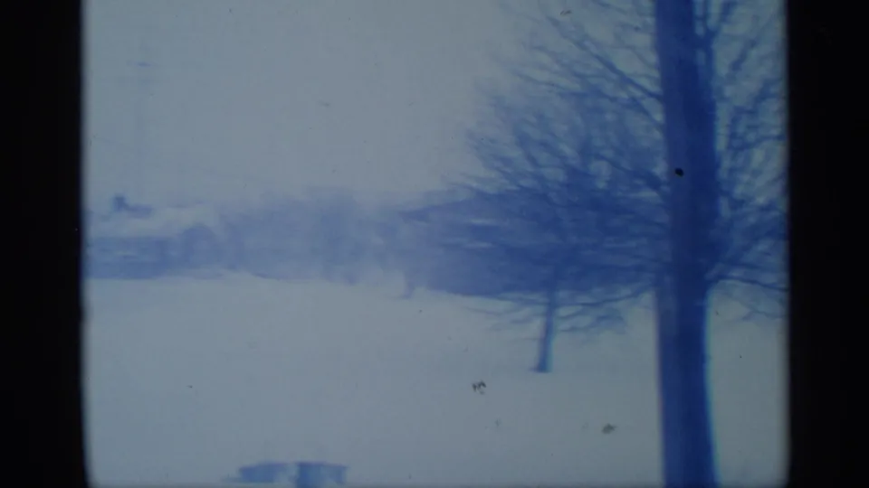 1959 New York winter landscape with snow, leafless trees, faint distant buildings, and heavy dark film or window edges.