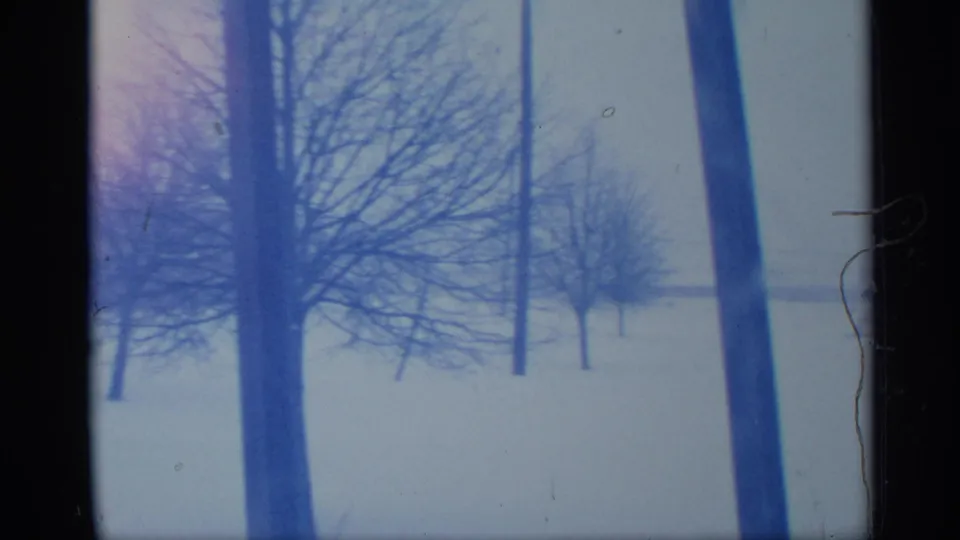 1959 New York home-movie frame with bare winter trees, utility poles, deep snow, and dark edge obstruction from the camera view.