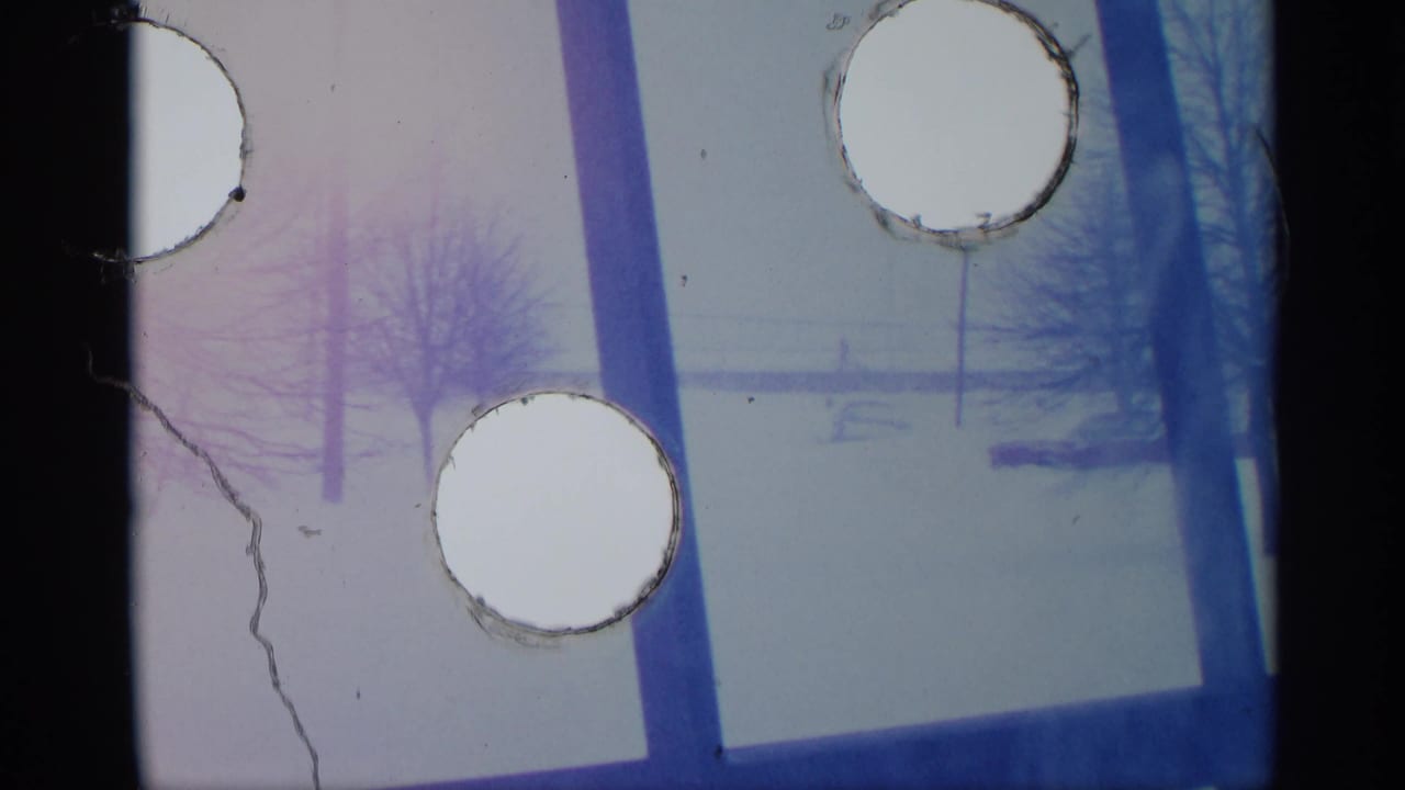 Snowy view through a window with bare trees and visible film perforation marks.