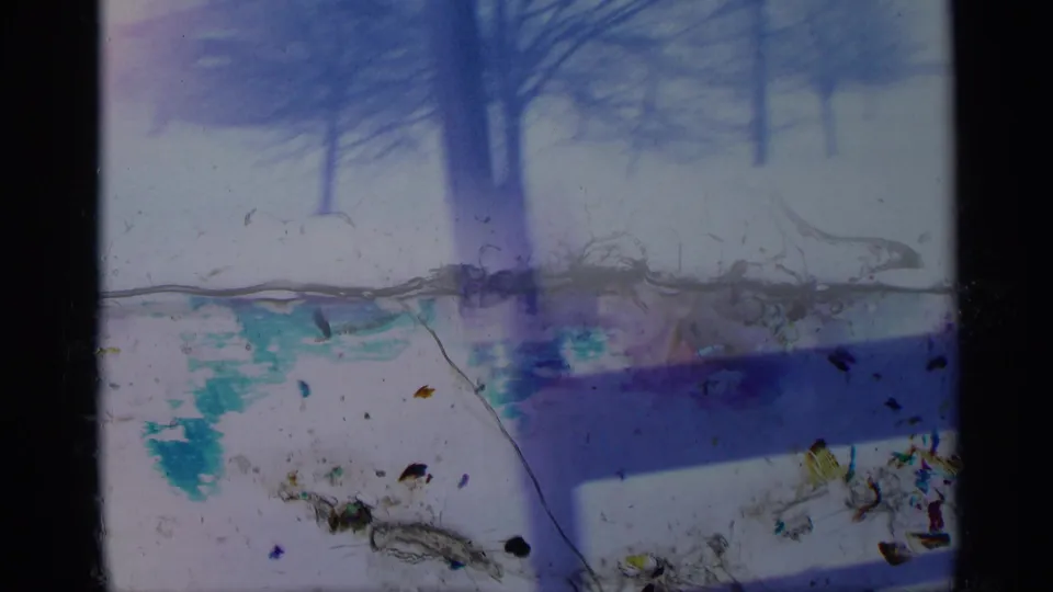 1959 New York home-movie frame looking through a window toward snow and trees, with pronounced 8mm wear and discoloration.
