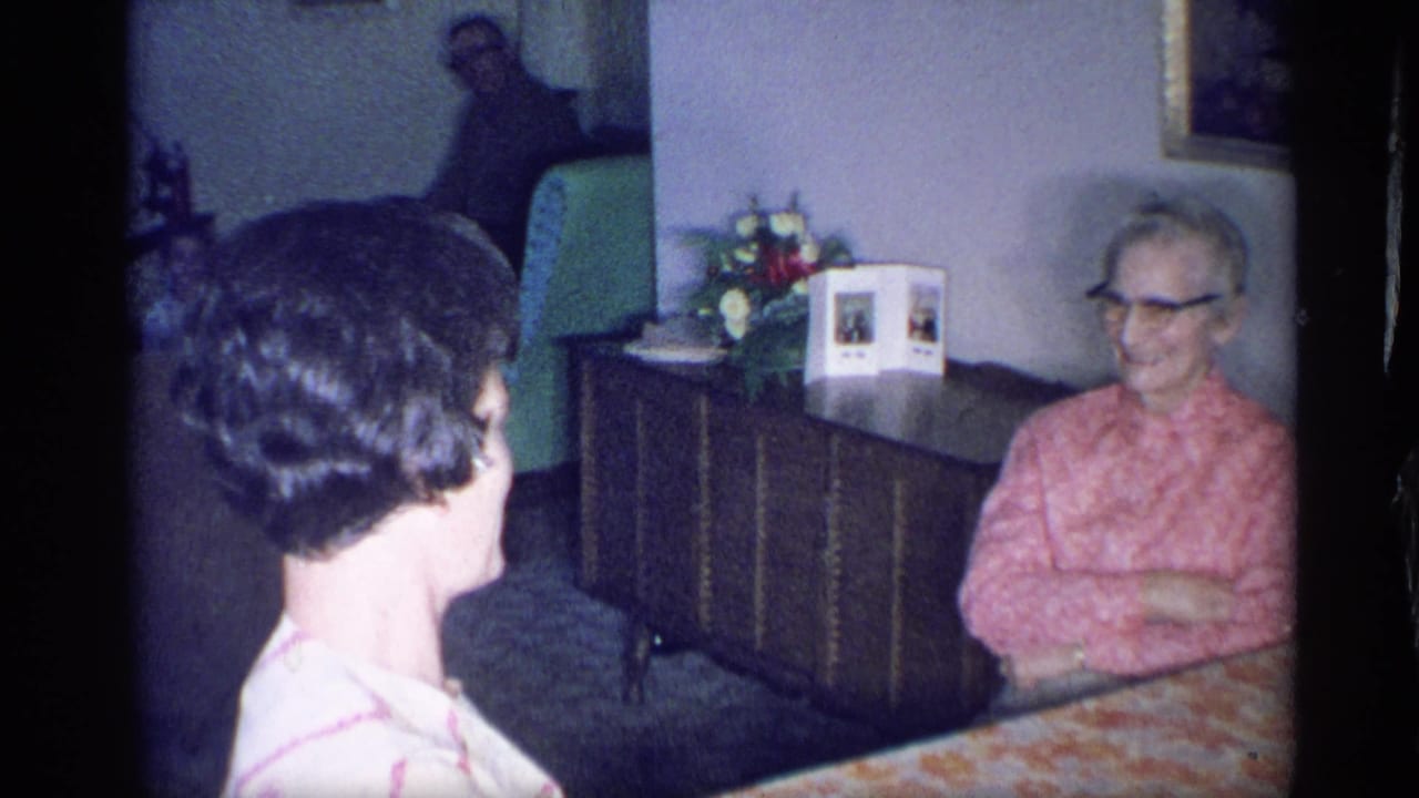 Younger woman faces an elderly woman seated at a table in a living room.